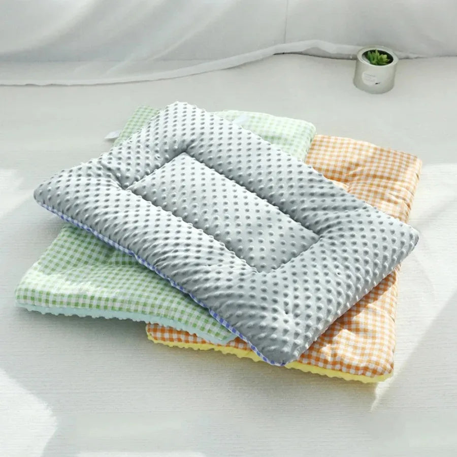 Grey dotted plush dog bed pad with a raised edge, stacked on green and orange gingham pads on a white floor