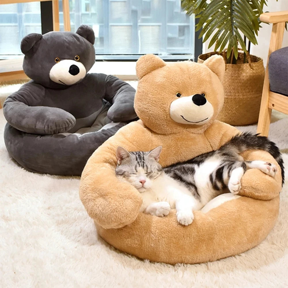 Tabby cat asleep in the tan teddy bear bed, the arms wrapped round it, with the grey version behind on a rug