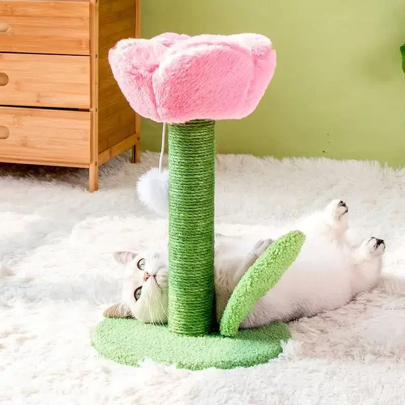 Pink tulip cat scratch post on a fluffy white rug, a white cat with grey ears lying on its back beside the sisal stem