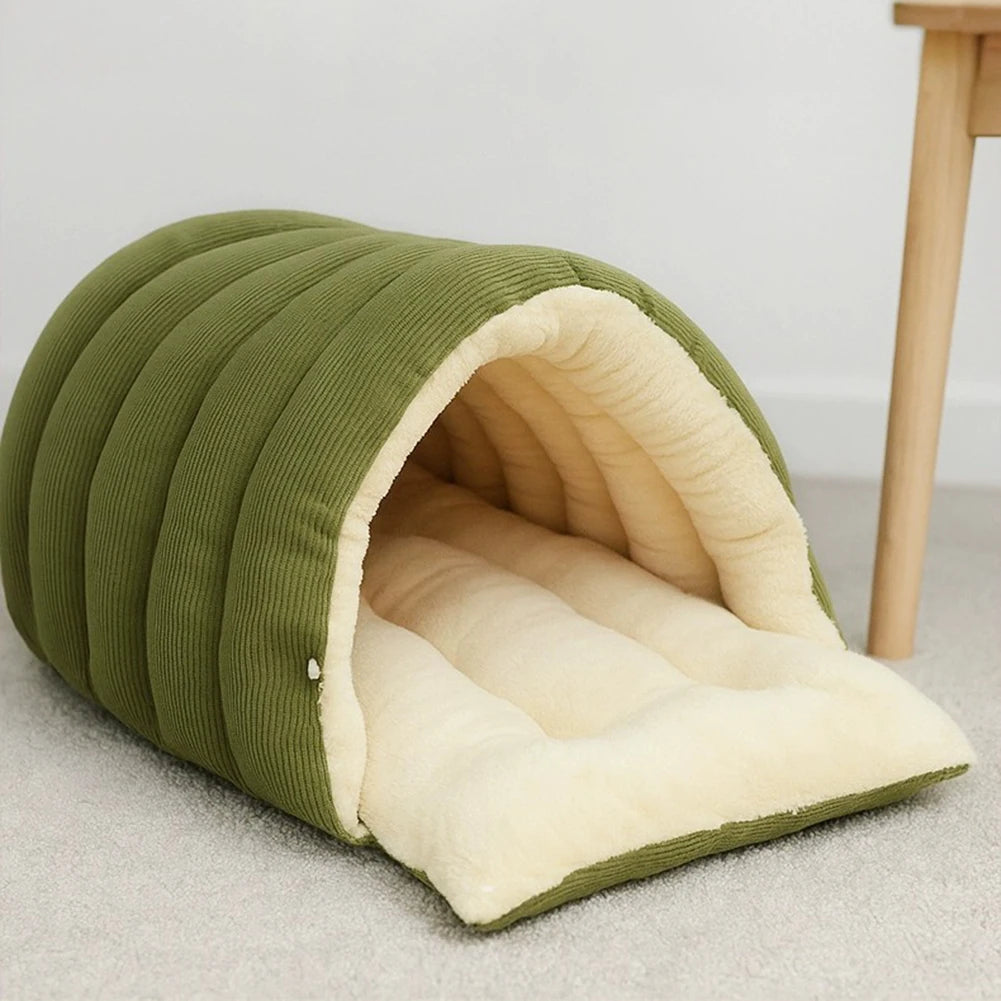 Green corduroy cave dog bed with its front flap folded down, showing the cream fleece lining, on a grey carpet