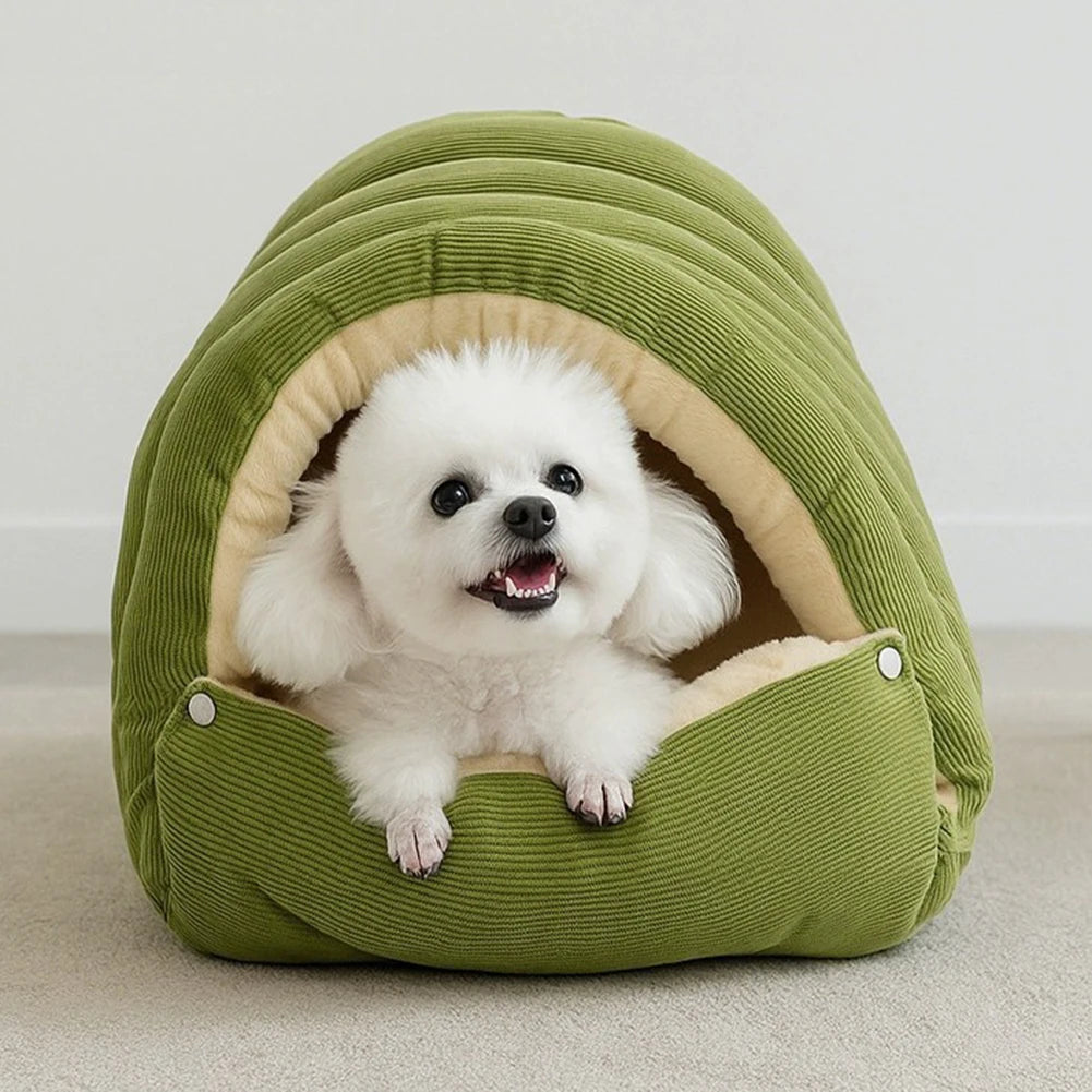Small fluffy white dog lying in the opening of a green corduroy cave dog bed, paws resting on the front flap