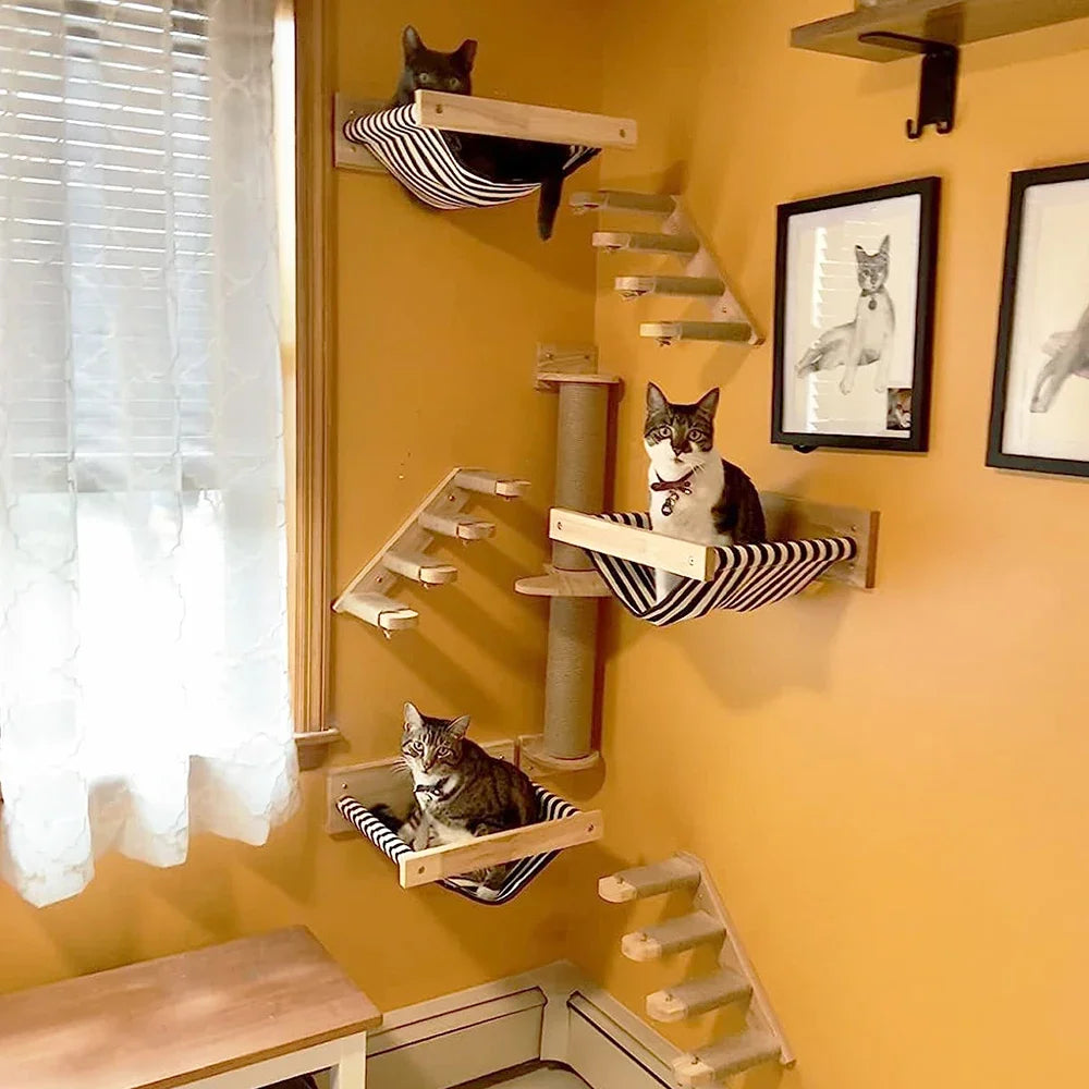 Corner cat tree on a yellow wall: striped hammocks, rope ladders and a sisal post, with three cats resting in the hammocks