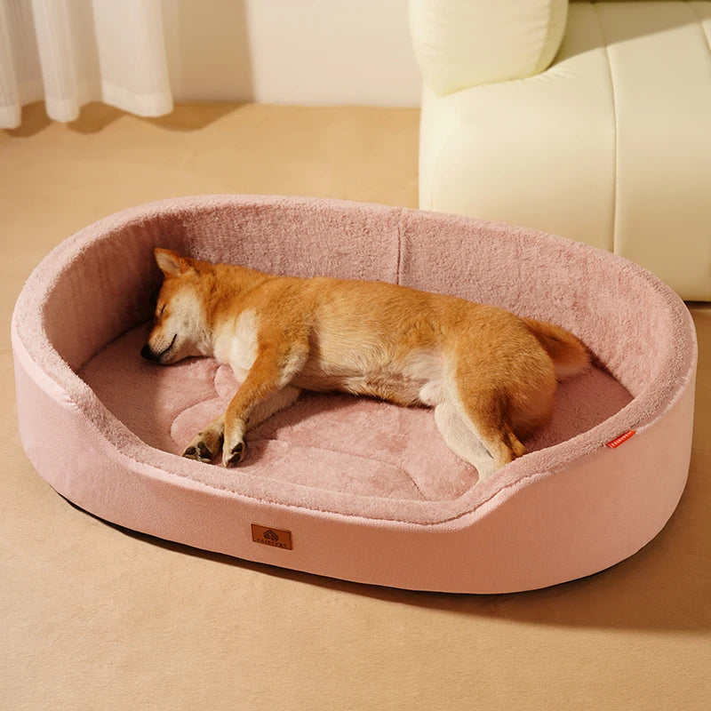 Shiba Inu asleep on its side in a pink oval basket dog bed, on a beige floor beside a cream sofa