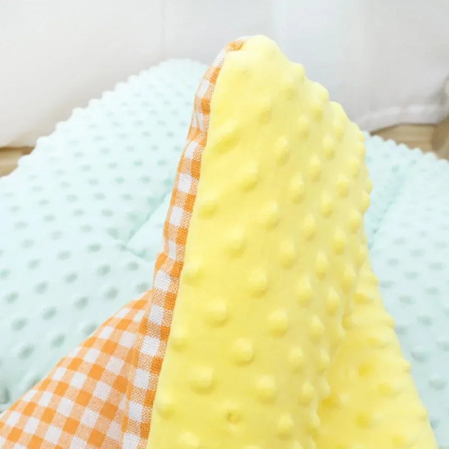 Close-up of the yellow dotted plush pad with its orange and white gingham reverse, on a mint pad