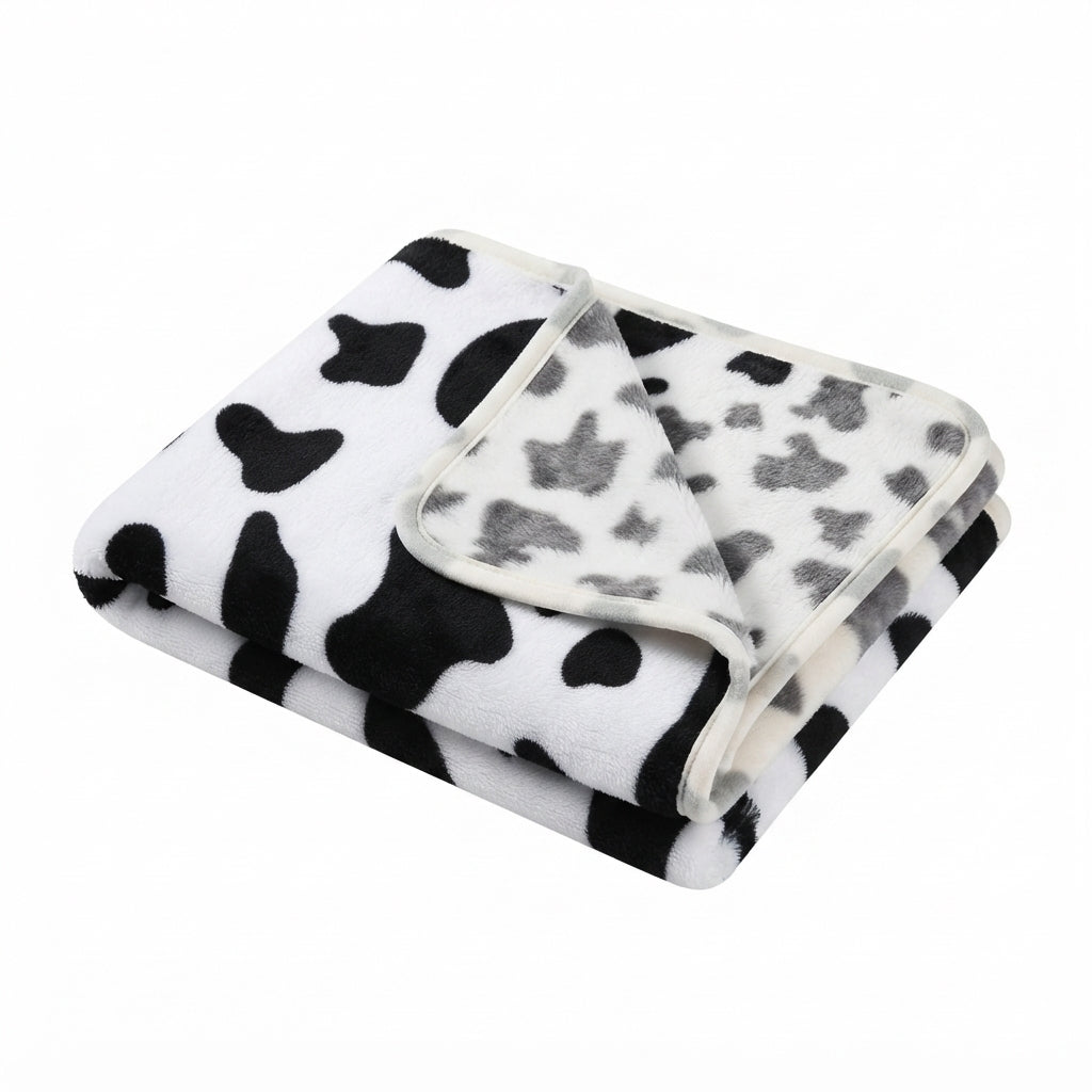 Folded white fleece blanket with a black cow print and grey patches on the reverse, cream edge