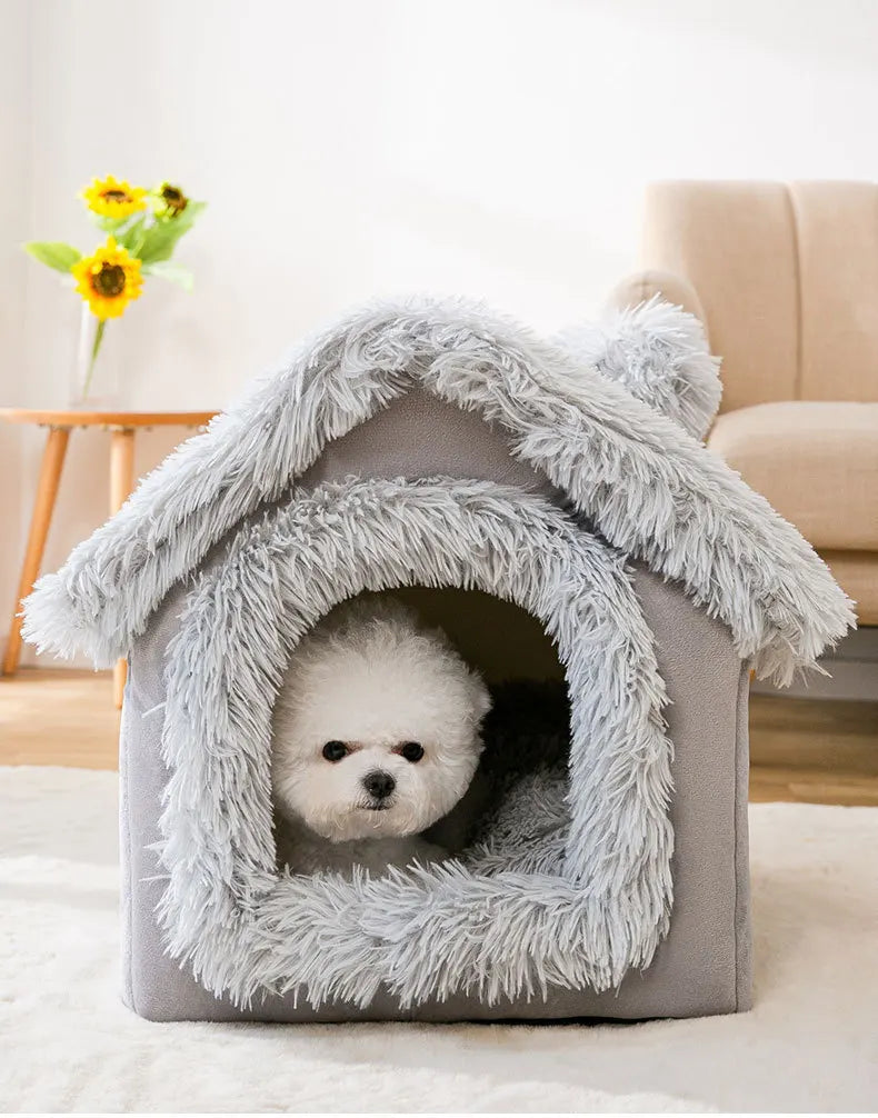 Grey long-plush house bed with a small white fluffy dog looking out of the door, in a living room