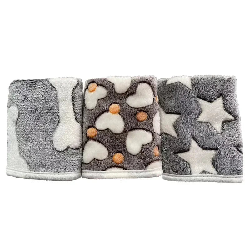 Fleece blanket for dog beds in three grey designs rolled side by side: white bones, hearts with orange dots, and stars