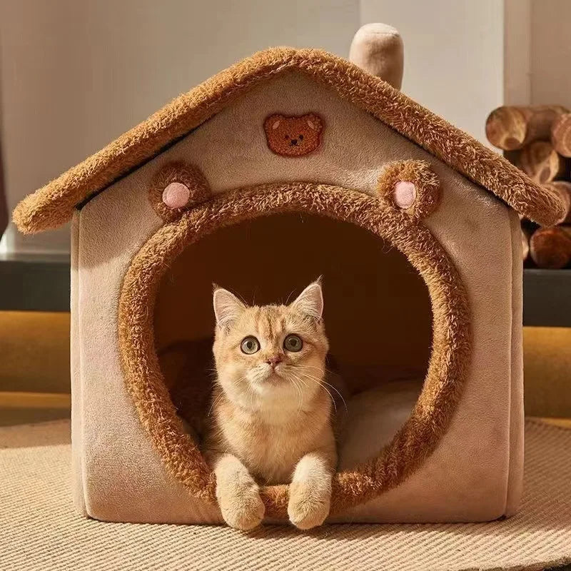 Brown bear-face cat bed house with a pitched roof, a ginger kitten sitting in the round doorway with its paws over the edge