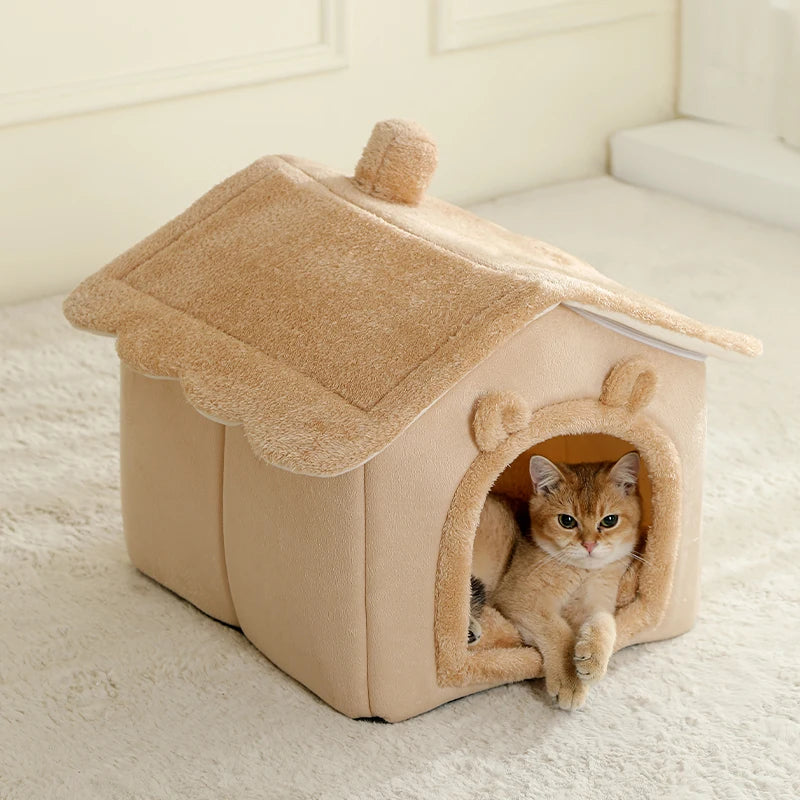 Ginger cat lying in the doorway of a brown house-shaped hooded pet bed with a plush roof, on a cream rug