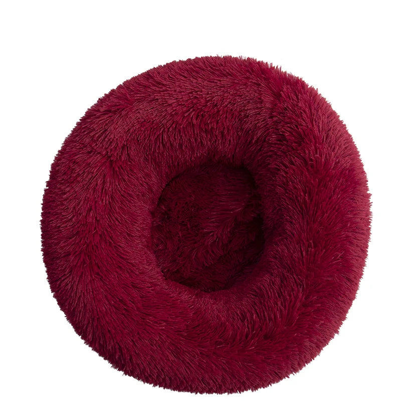 Round donut dog bed in burgundy shaggy plush, a deep wine red with a central hollow, seen from above