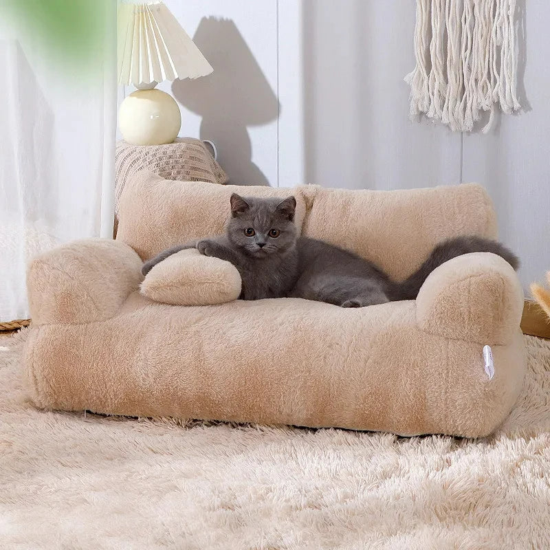 Grey kitten lying on a camel plush sofa cat bed, one paw on the small pillow, on a fluffy cream rug