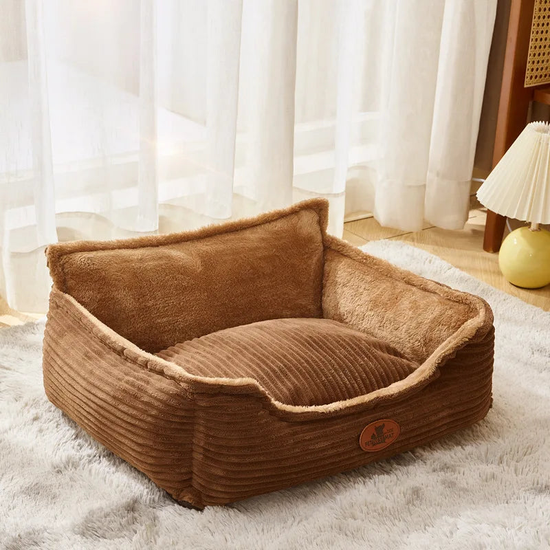 Coffee brown corduroy nest dog bed on a grey shaggy rug by a window with white curtains and a small lamp