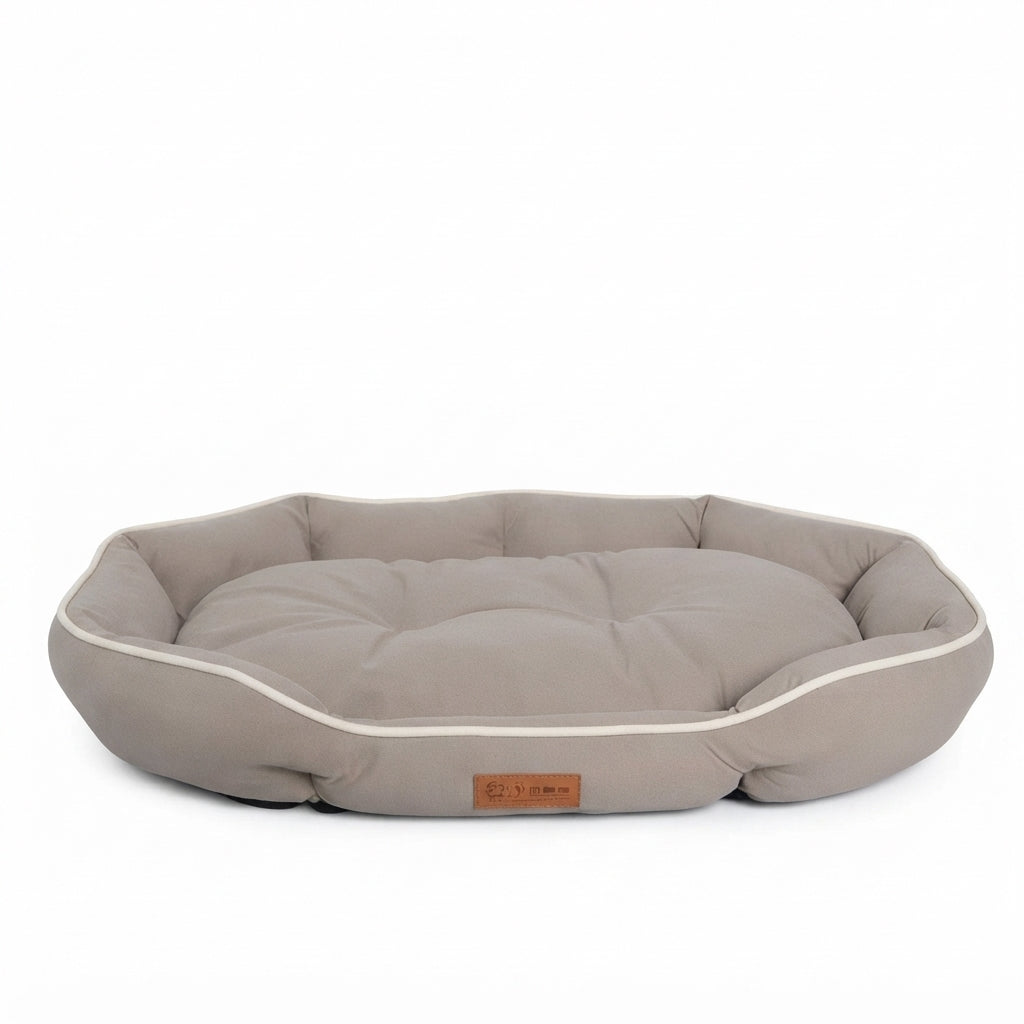 Octagonal dog bed in khaki, a greyish taupe fabric, with cream piping and a padded rim around a tufted cushion