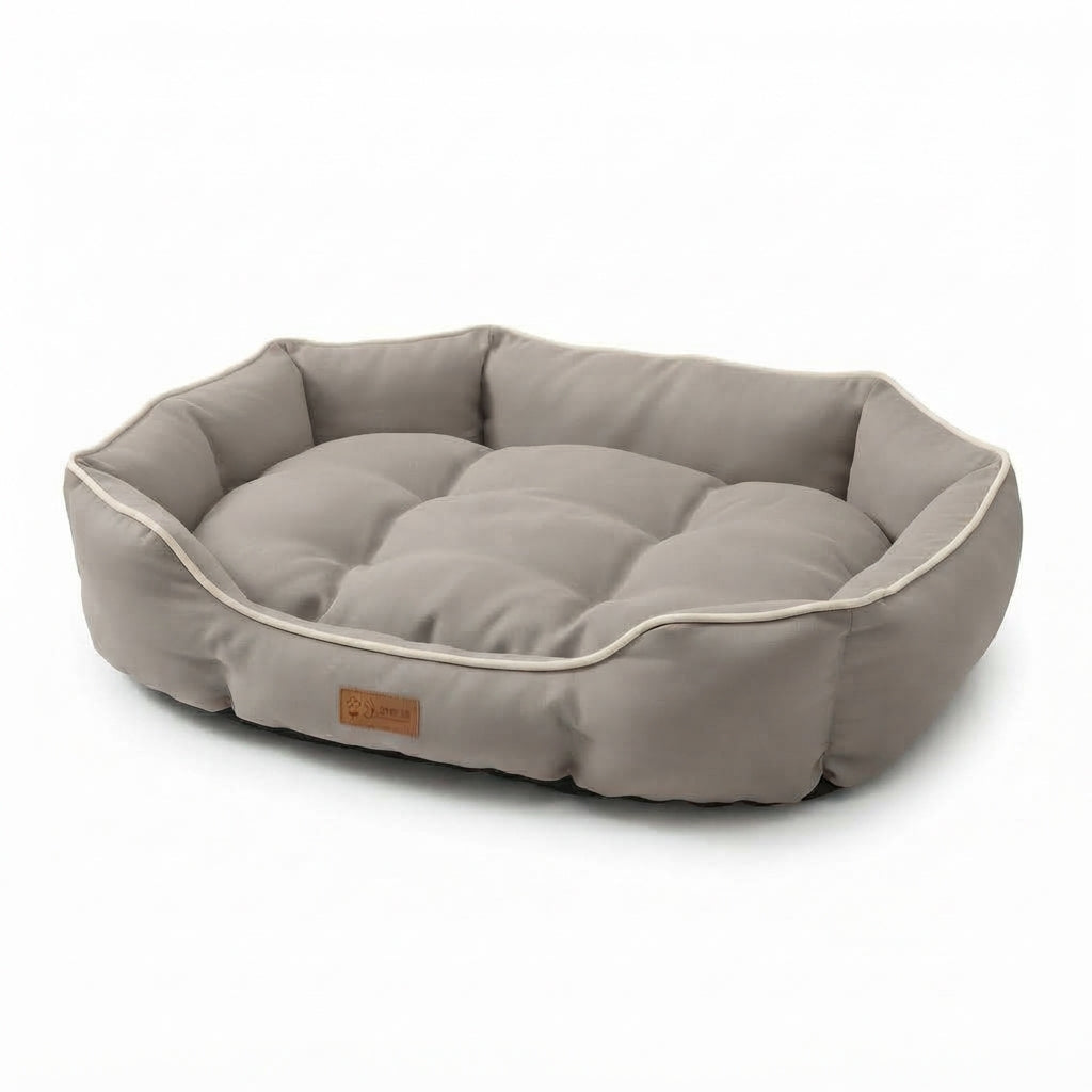 Small oval dog bed in beige suede-look fabric with cream piping, raised sides and a tufted cushion