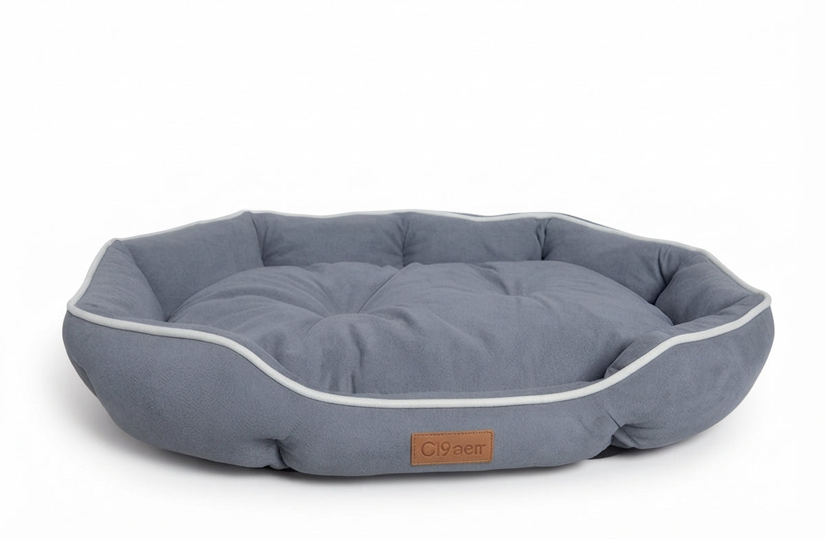 Small oval dog bed in blue-grey suede-look fabric with white piping and a tufted cushion