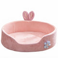 Pink bed for dogs with bunny ears: a round, high-sided plush bed with a pale blue flower on the front
