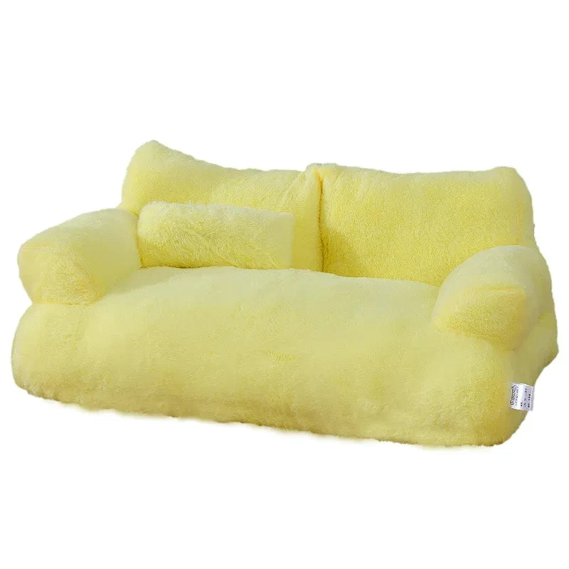 Plush two-seater sofa cat bed in pale yellow faux fur with rounded armrests, a split backrest and a small pillow