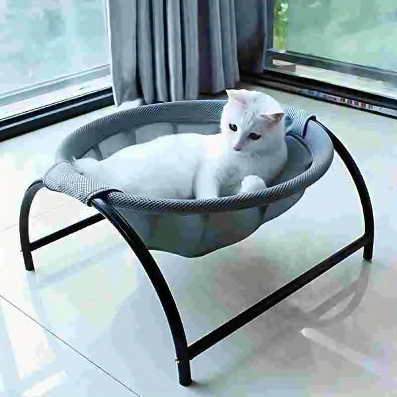 White cat lying in a grey mesh round cat hammock bed on a black arch frame, on a tiled floor by a window