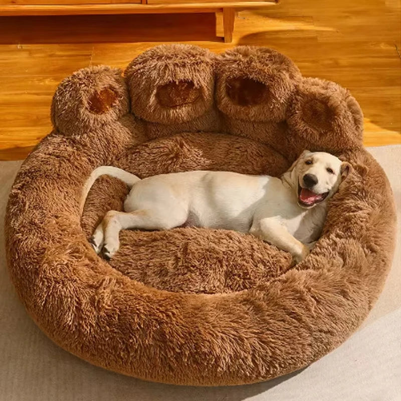 Pale yellow puppy lying on its side in a brown paw-shaped round dog bed on a wooden floor