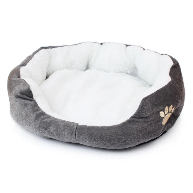 Oval pet bed in grey with a white fleece lining, a raised rim and a beige embroidered paw print