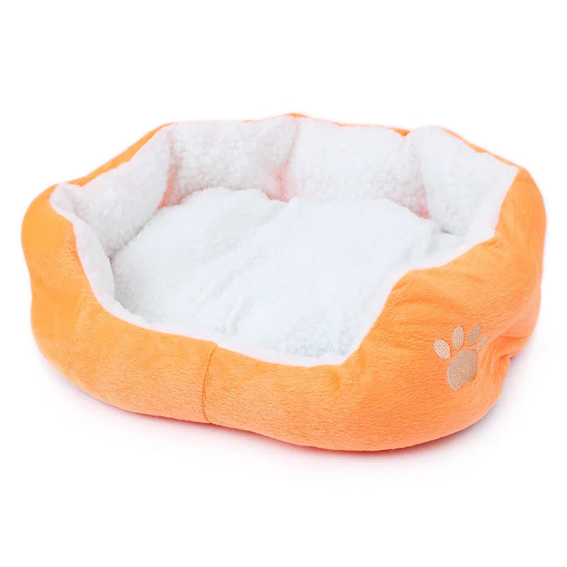 Oval pet bed in orange with a white fleece lining and a beige embroidered paw print on the side
