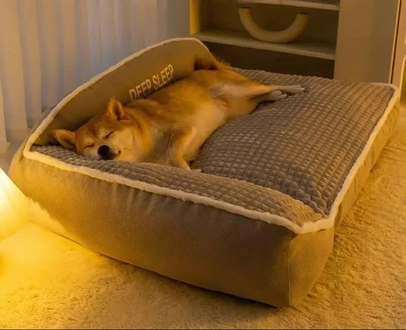 Shiba Inu asleep on its back against the raised backrest of a grey sofa-style dog bed with a waffle-textured top