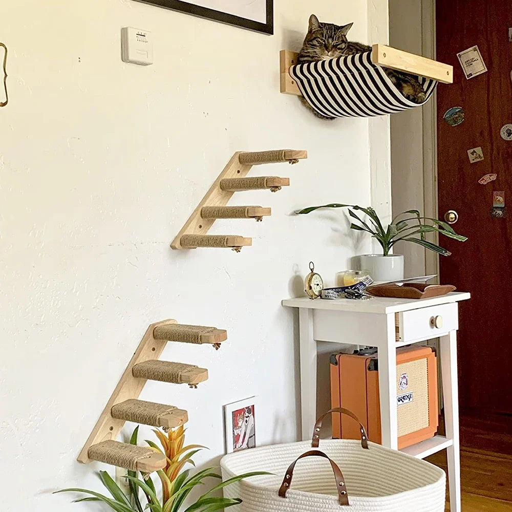 Tabby cat lying in a black and white striped wall hammock above two wooden ladders with rope-wrapped steps
