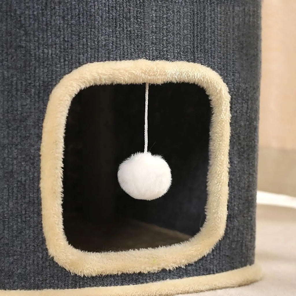 Close-up of a square doorway with beige plush trim and a white pompom hanging inside the grey cat house