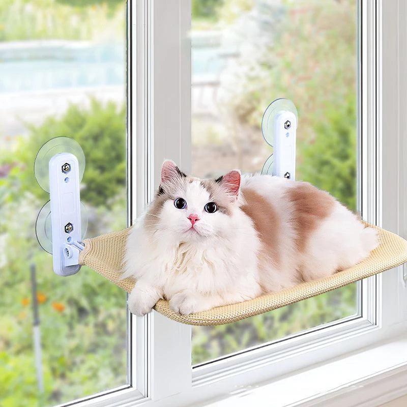 Fluffy white and brown cat lying on a light yellow mesh window cat bed stuck to a window by suction cups, a garden outside